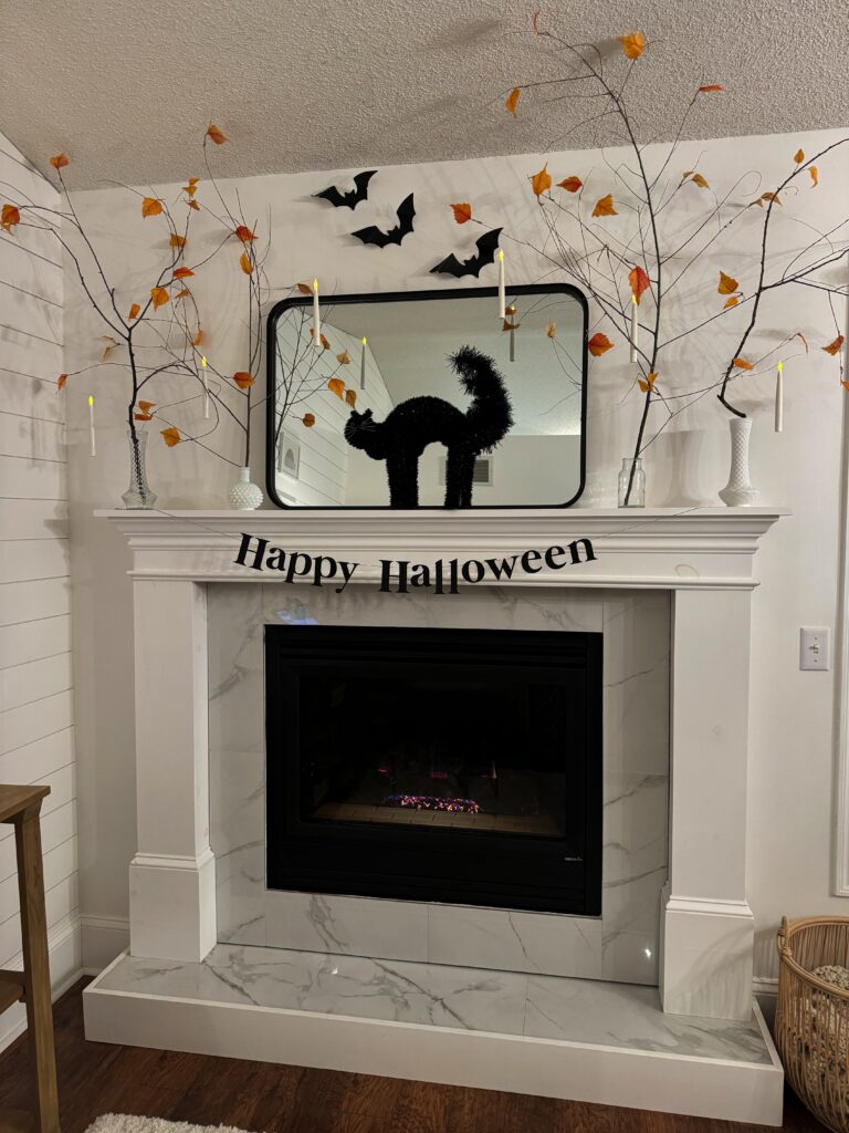 a nature inspired Halloween mantel in the stir and gather blog house with branches, bats, hanging candles and a spooky black cat